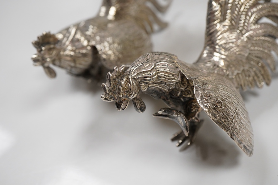 A pair of modern silver fighting cocks, import marks for Sheffield, Assay Office, Sheffield, 1977, height 68mm, together with a Chinese white metal miniature model of a ship, on a carved hardwood base, overall height 20.